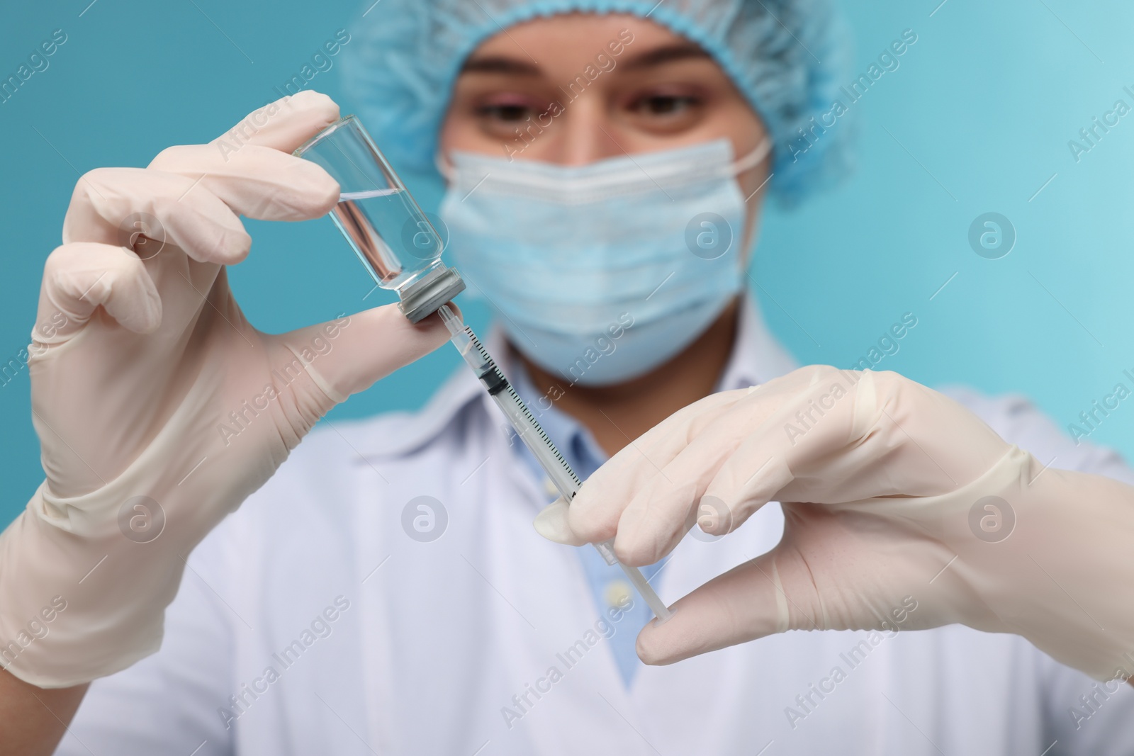 Photo of Doctor filling syringe with medication from glass vial on light blue background, selective focus