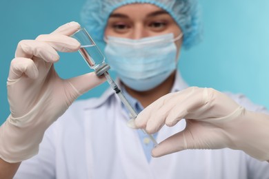 Doctor filling syringe with medication from glass vial on light blue background, selective focus