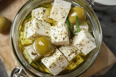 Photo of Top view of pickled feta cheese in jar on grey table, closeup