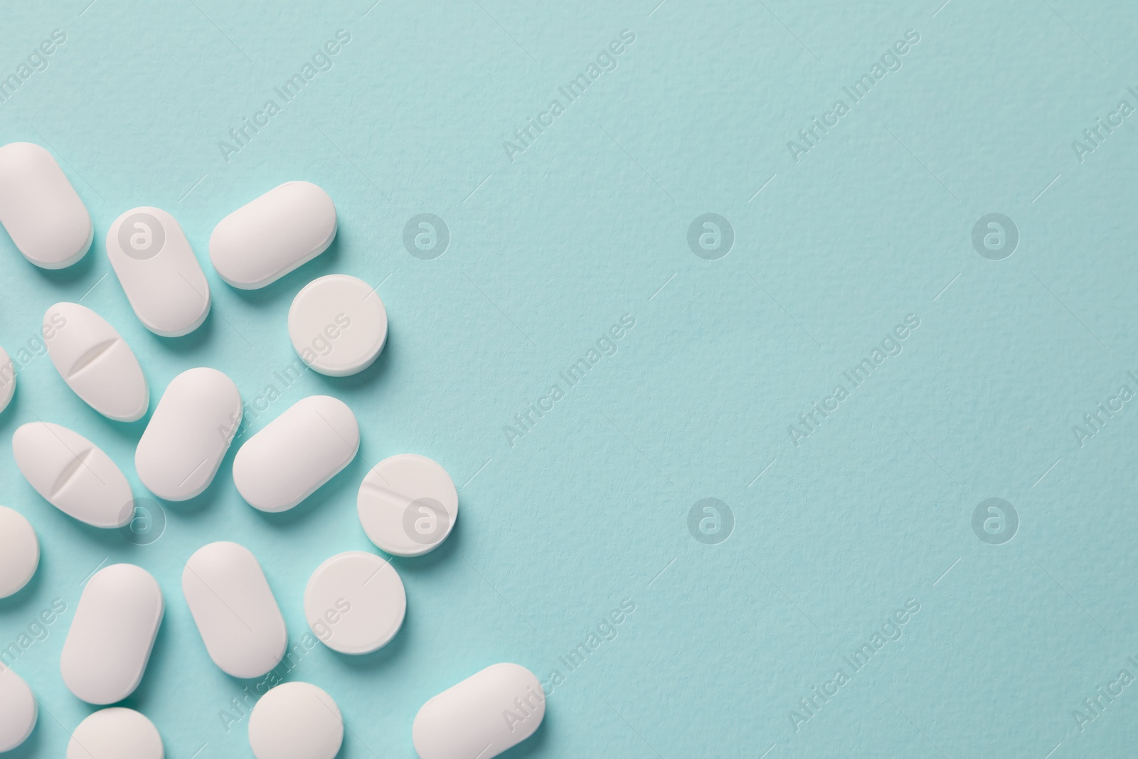 Photo of White pills on mint background, flat lay. Space for text