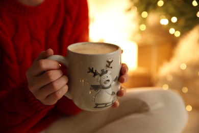 Woman with cup of drink and blurred Christmas lights on background, closeup