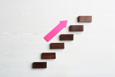 Photo of Stairs made of blocks and pink arrow on white wooden background, flat lay. Career promotion concept