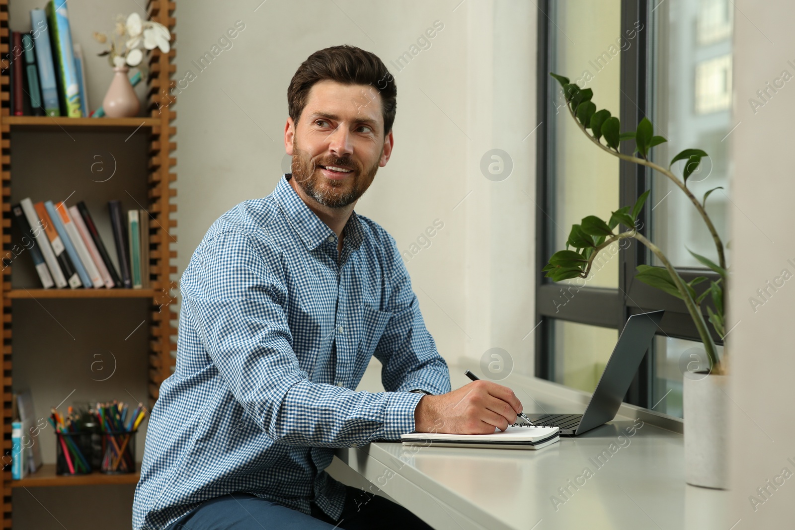 Photo of Man writing something and laptop at table in cafe