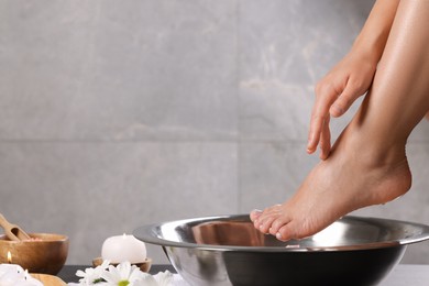 Photo of Woman soaking her foot in bowl with water on dark surface, closeup. Pedicure procedure