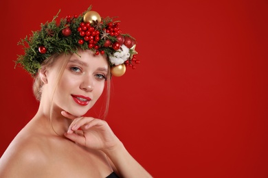 Beautiful young woman wearing Christmas wreath on red background. Space for text