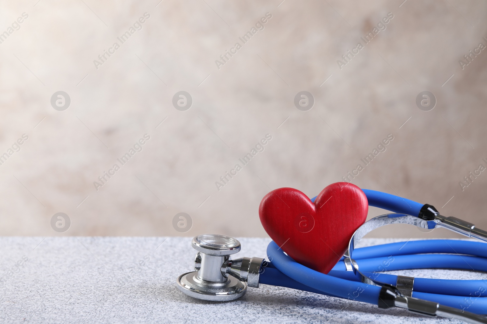 Photo of Stethoscope and red heart on grey stone table, closeup. Space for text