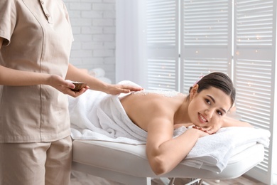 Photo of Young woman having body scrubbing procedure with sea salt in spa salon