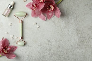 Photo of Natural jade face roller, cosmetic product and flowers on grey background, flat lay. Space for text