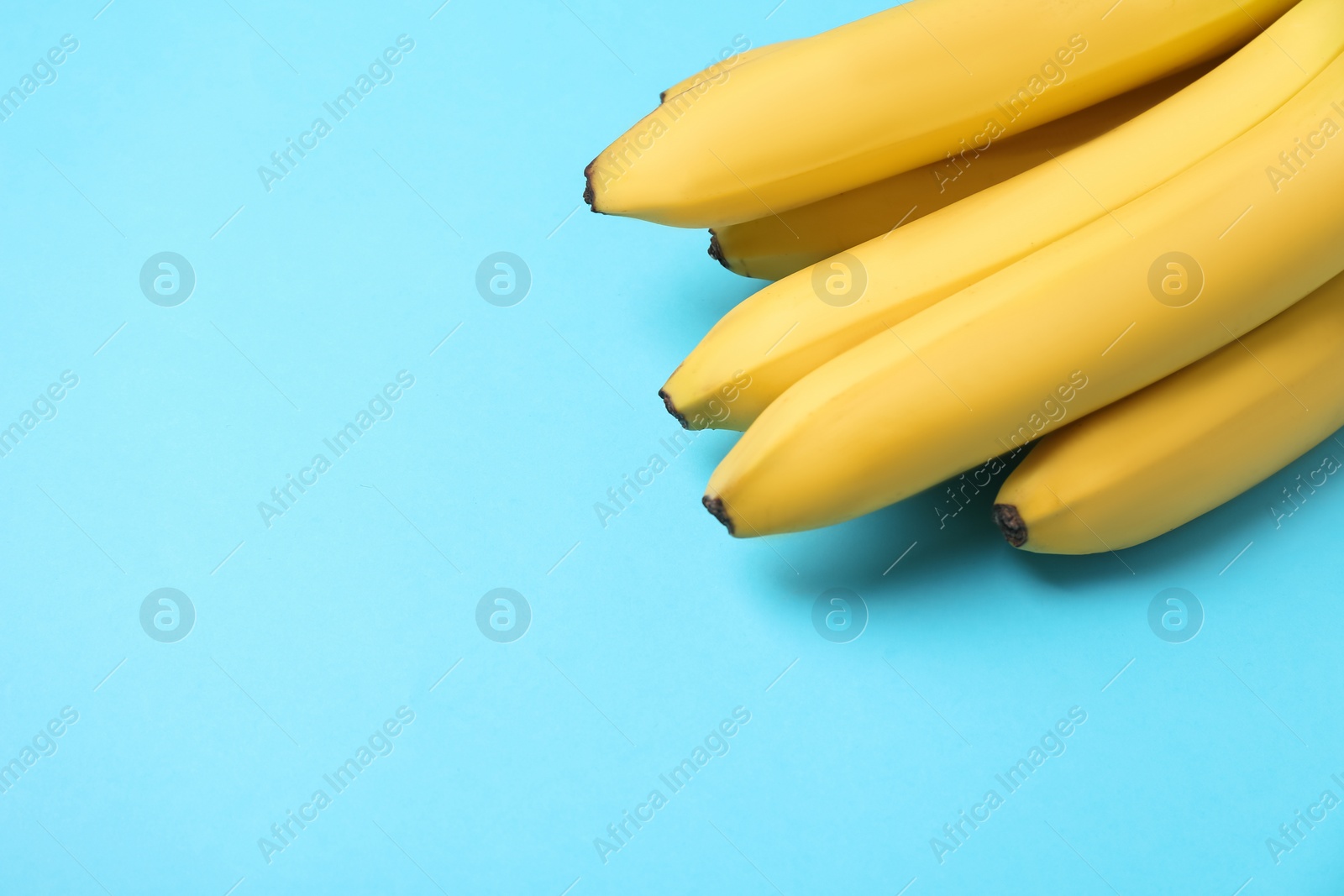 Photo of Ripe yellow bananas on turquoise background, closeup. Space for text