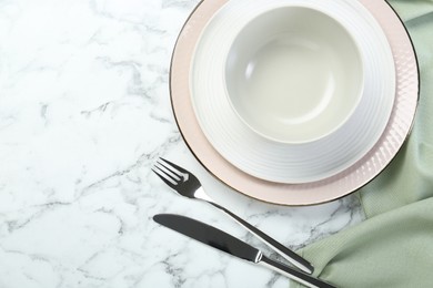 Clean plates, bowl and cutlery on white marble table, flat lay. Space for text