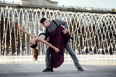 Beautiful young couple practicing dance moves near fountain outdoors
