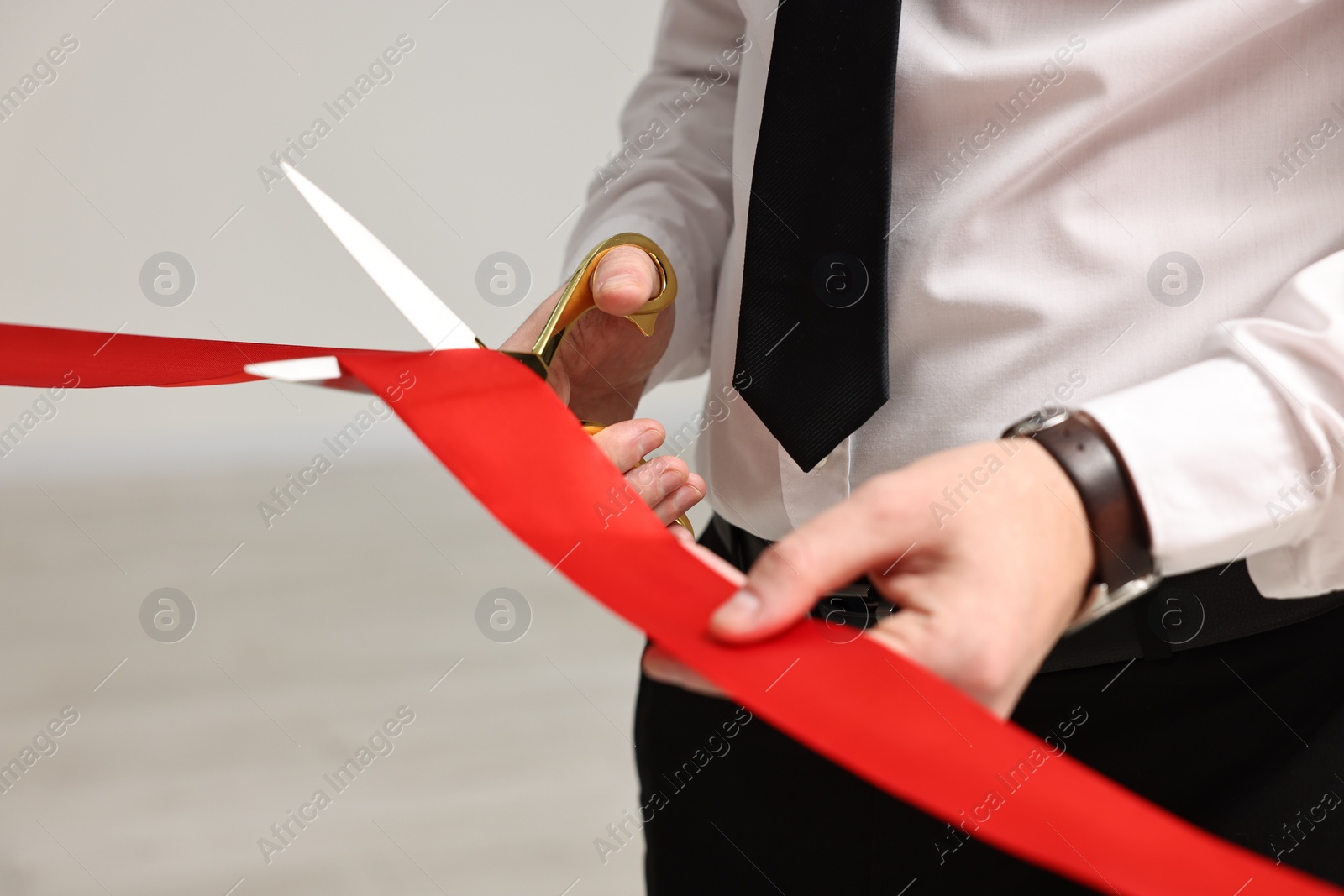 Photo of Man cutting red ribbon with scissors on blurred background, closeup