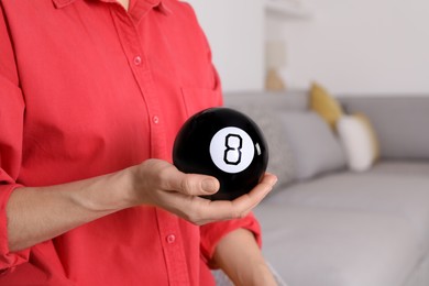 Photo of Woman holding magic eight ball indoors, closeup