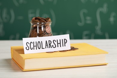 Photo of Scholarship concept. Sheet of paper, glass jar with coins and book on white wooden table