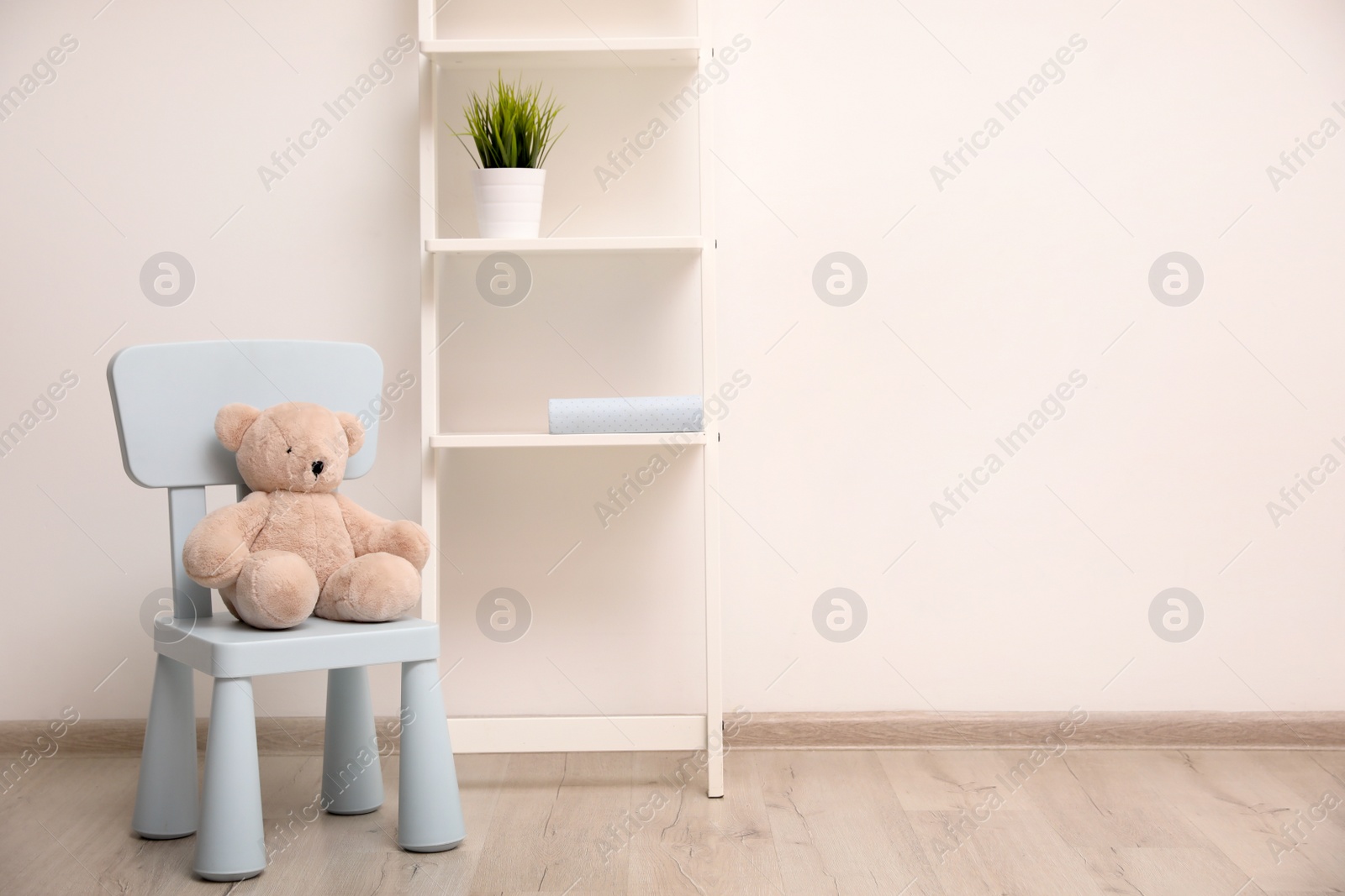 Photo of Teddy bear on chair and shelving unit near wall in child room. Space for text