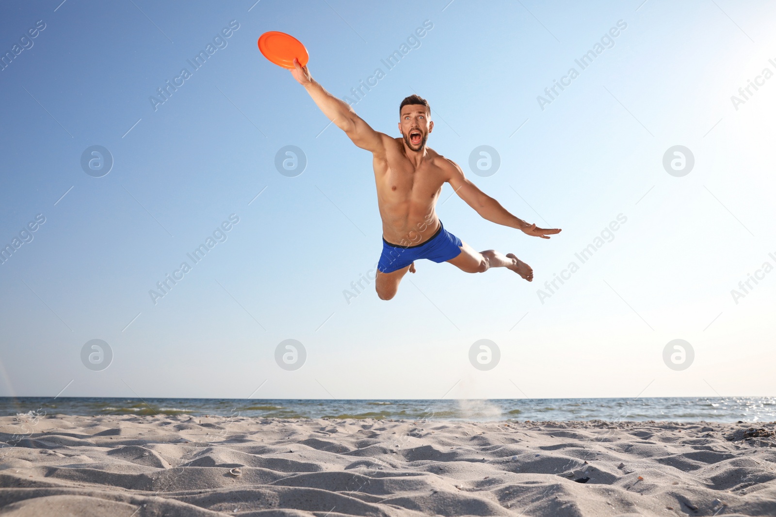 Photo of Sportive man jumping and catching flying disk at beach