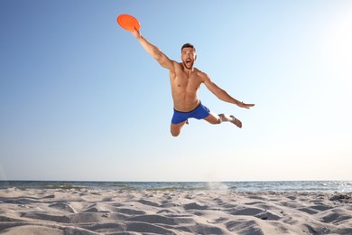 Photo of Sportive man jumping and catching flying disk at beach