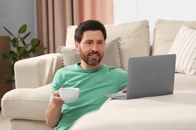 Man with cup of drink using laptop at home