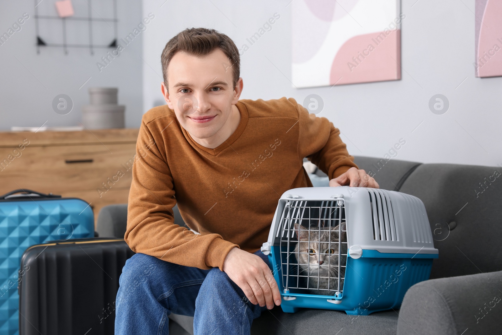 Photo of Travel with pet. Man near carrier with cute cat on sofa at home