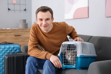 Photo of Travel with pet. Man near carrier with cute cat on sofa at home