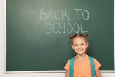 Photo of Little child near chalkboard with text BACK TO SCHOOL