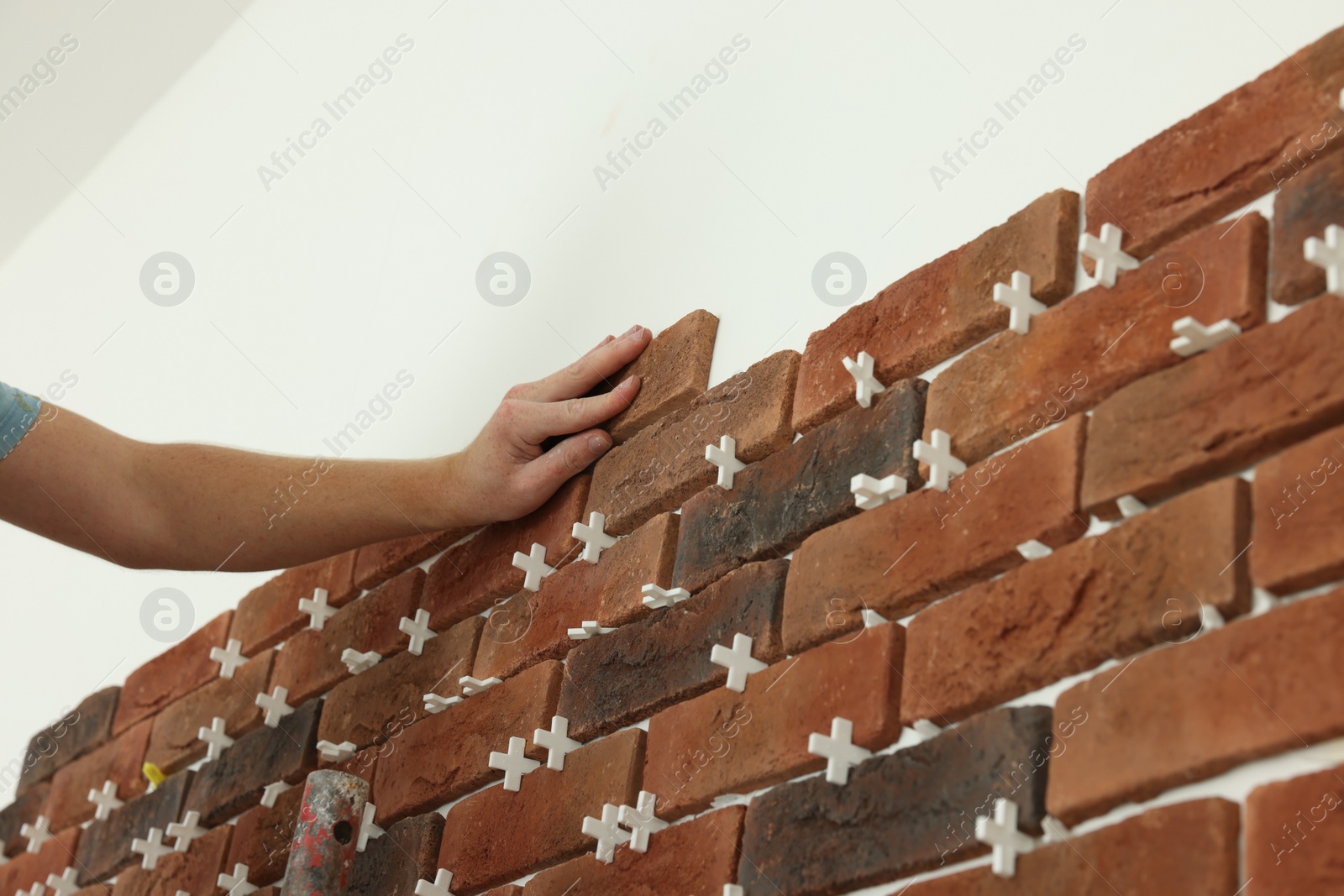 Photo of Professional builder gluing decorative brick on wall, closeup. Tiles installation process