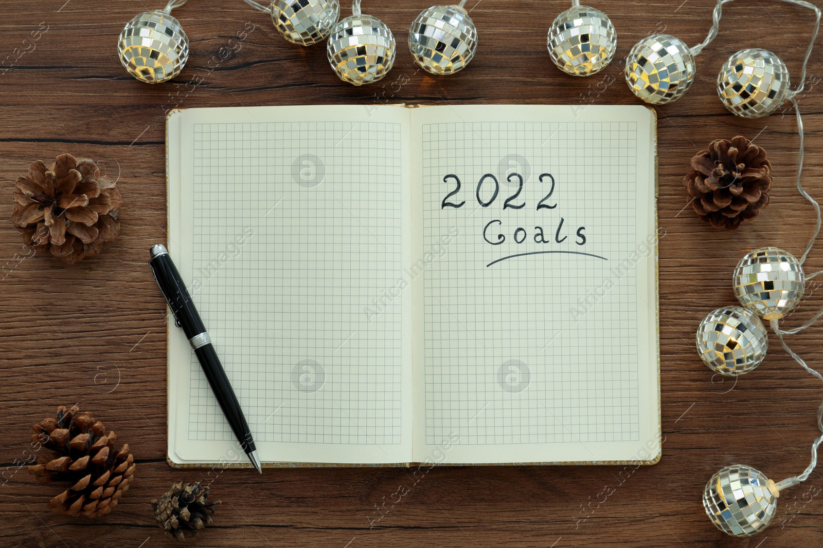 Photo of Open planner, pen, pine cones and Christmas lights on wooden table, flat lay. Planning for 2022 New Year