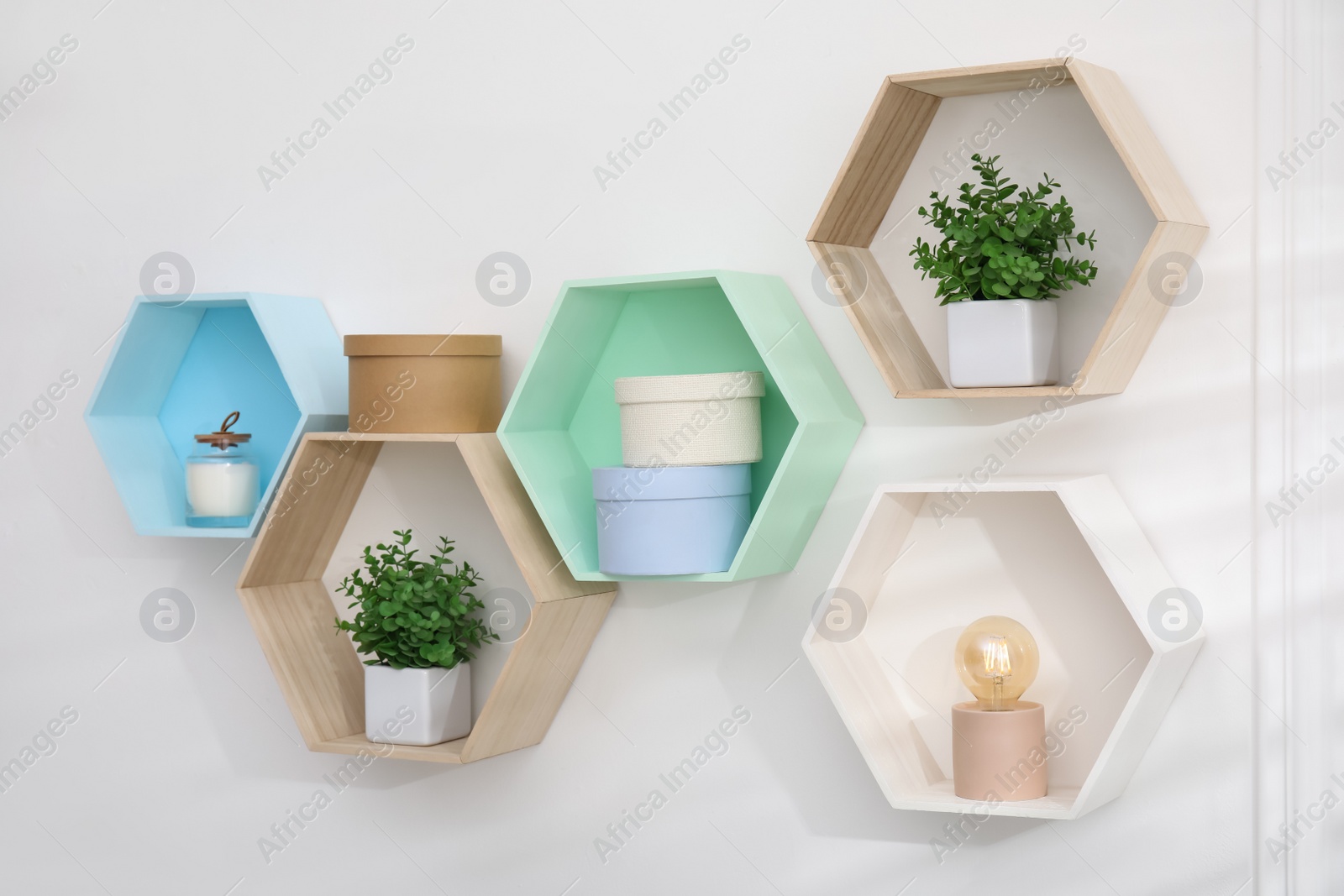 Photo of Honeycomb shaped shelves with decorative elements and houseplants on white wall