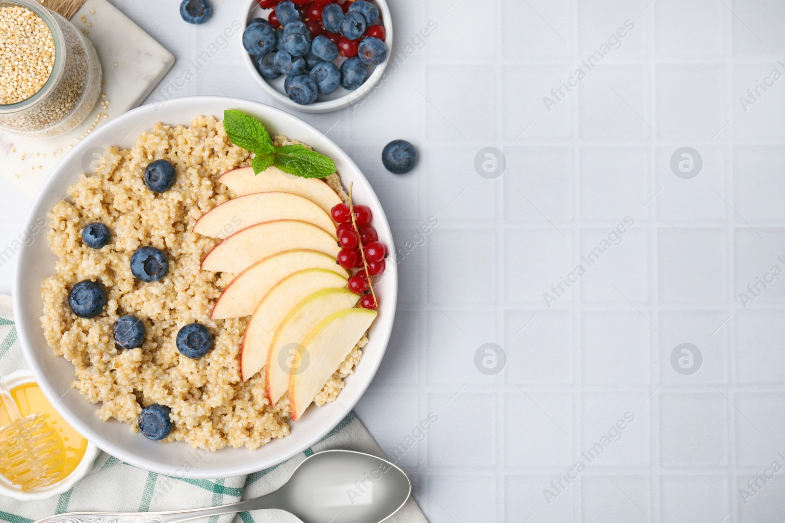 Photo of Bowl of delicious cooked quinoa with apples, blueberries and cranberries on white tiled table, flat lay. Space for text