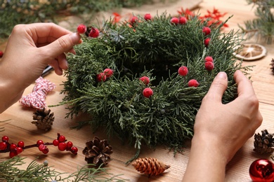 Photo of Florist making beautiful Christmas wreath with berries at wooden table, closeup