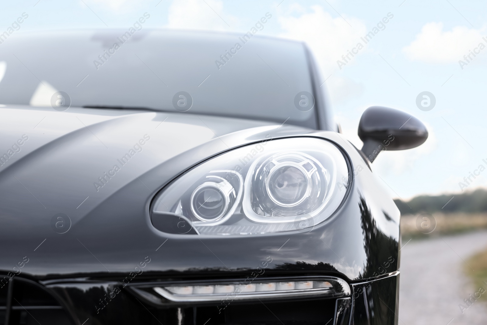 Photo of Modern black car parked outdoors, closeup view of headlight