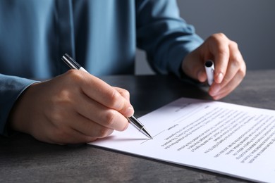 Photo of Woman signing document with pen at grey table, closeup