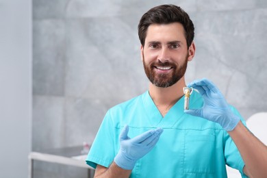 Photo of Dentist holding educational model of dental implant in clinic. Space for text