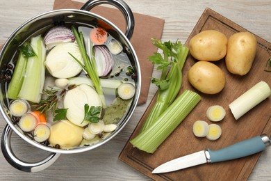 Pot and different ingredients for cooking tasty bouillon on white wooden table, flat lay