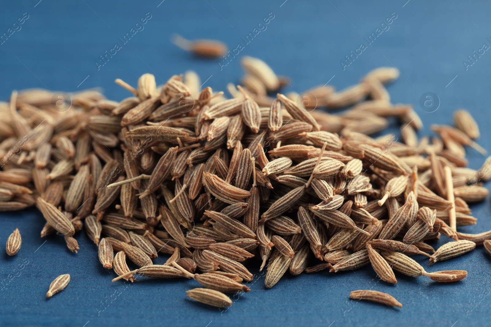 Photo of Pile of caraway seeds on blue wooden table, closeup