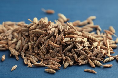 Pile of caraway seeds on blue wooden table, closeup