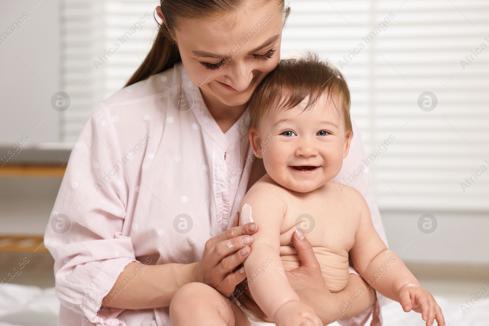 Photo of Happy mother applying body cream onto baby`s skin at home