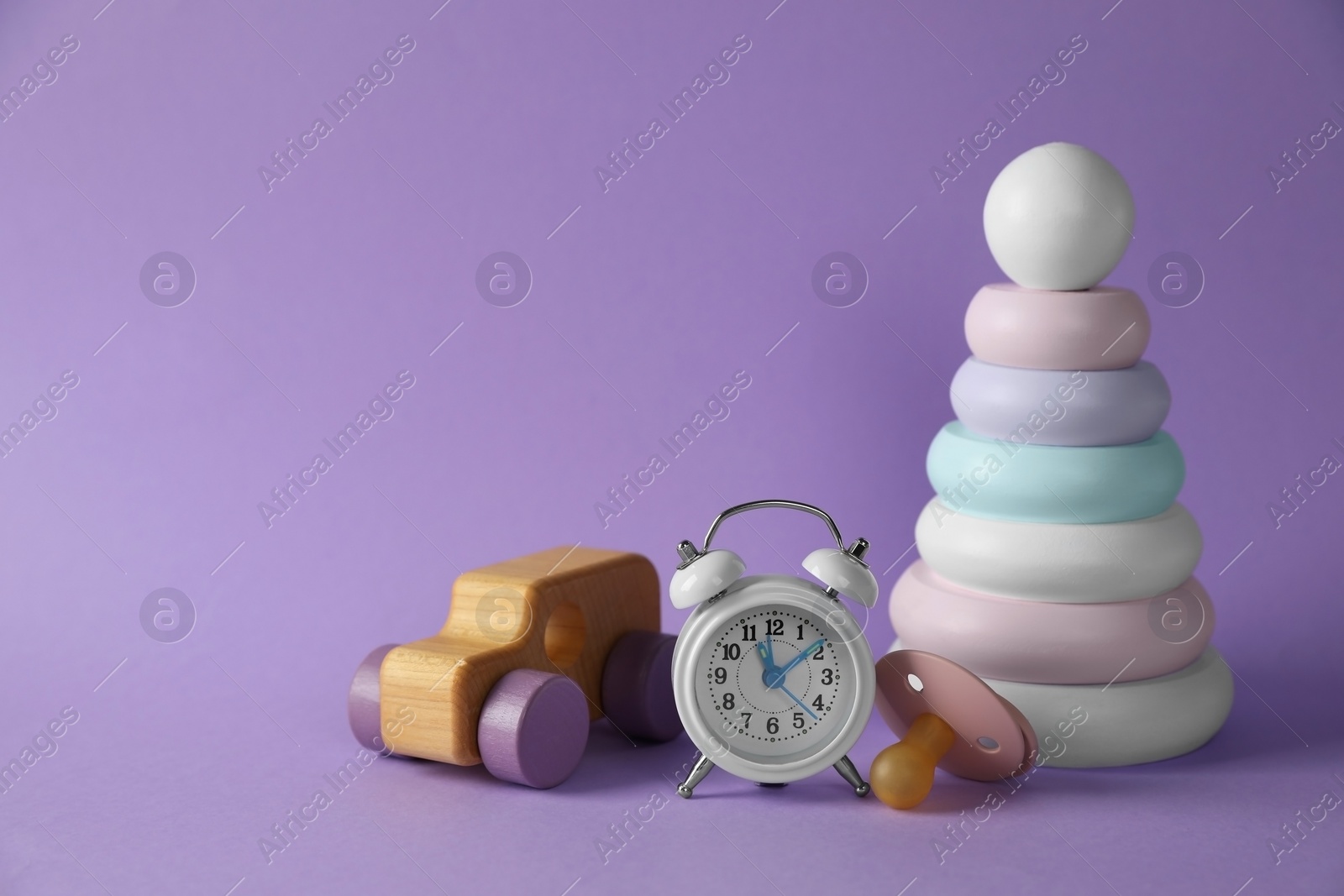 Photo of Alarm clock, toys and baby dummy on violet background, space for text. Time to give birth