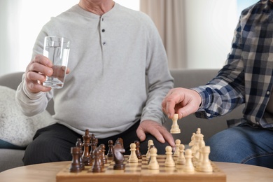 Elderly men playing chess at nursing home, closeup. Assisting senior people
