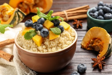 Photo of Tasty quinoa porridge with blueberries, pumpkin and mint in bowl on wooden table, closeup