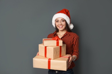 Young woman with Christmas gifts on grey background