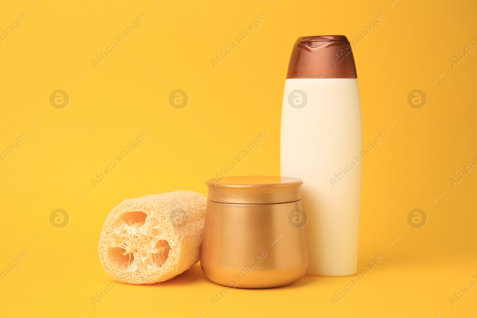 Photo of Natural loofah sponge and cosmetic products on yellow background