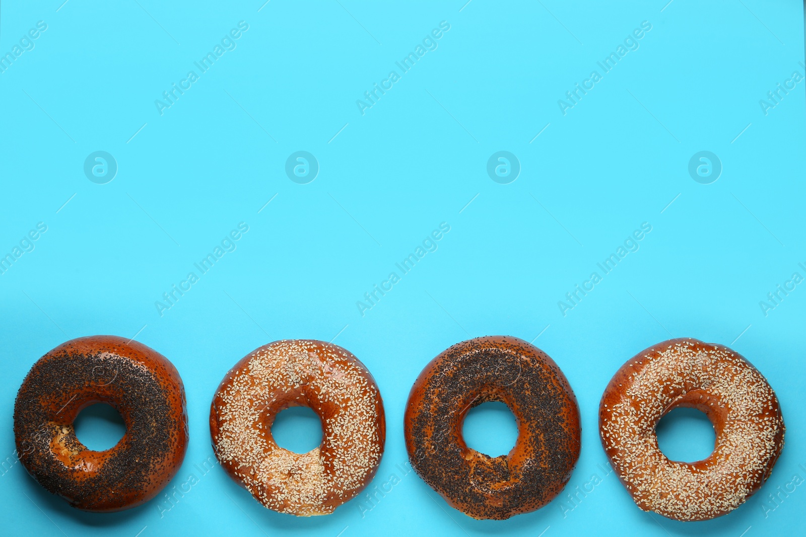 Photo of Many delicious fresh bagels on light blue background, flat lay. Space for text