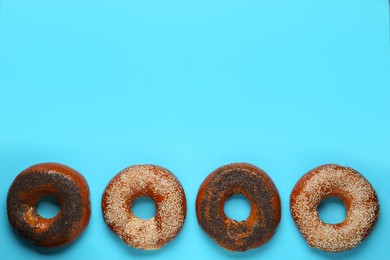 Many delicious fresh bagels on light blue background, flat lay. Space for text