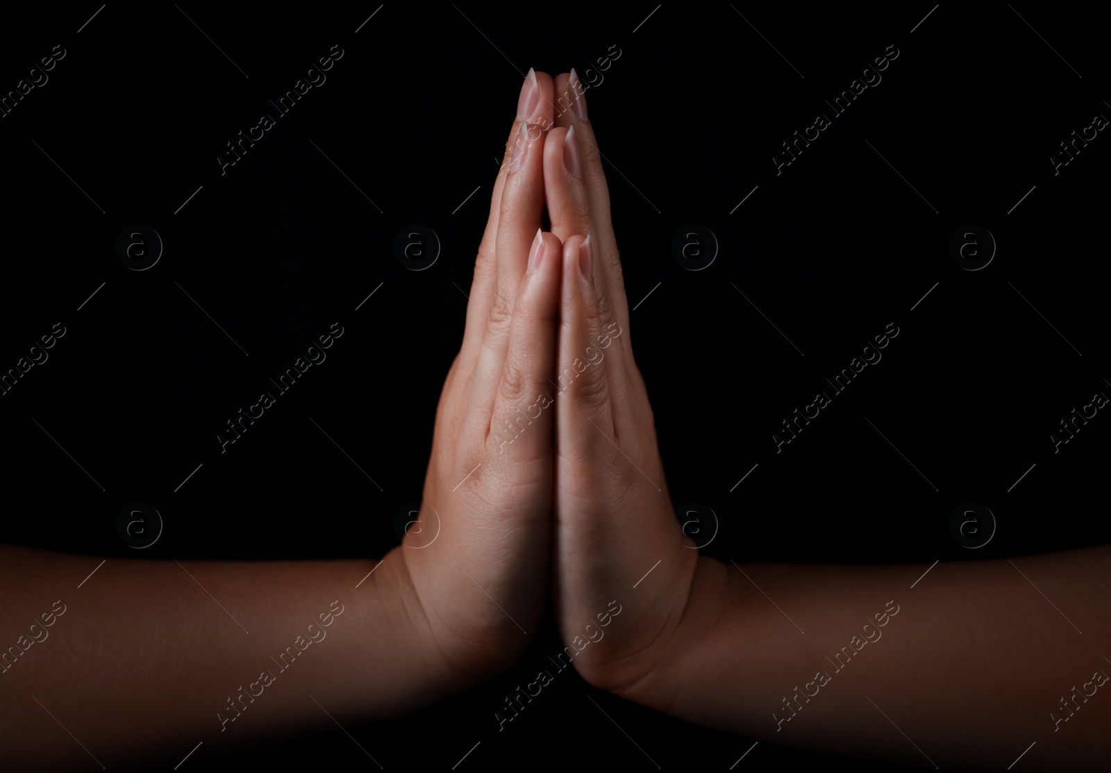 Photo of Woman holding hands clasped while praying against black background, closeup