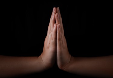 Photo of Woman holding hands clasped while praying against black background, closeup