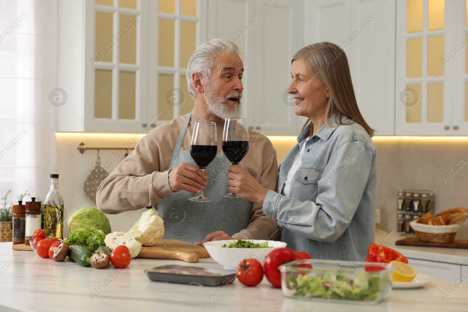 Photo of Happy senior couple with glasses of wine cooking together in kitchen