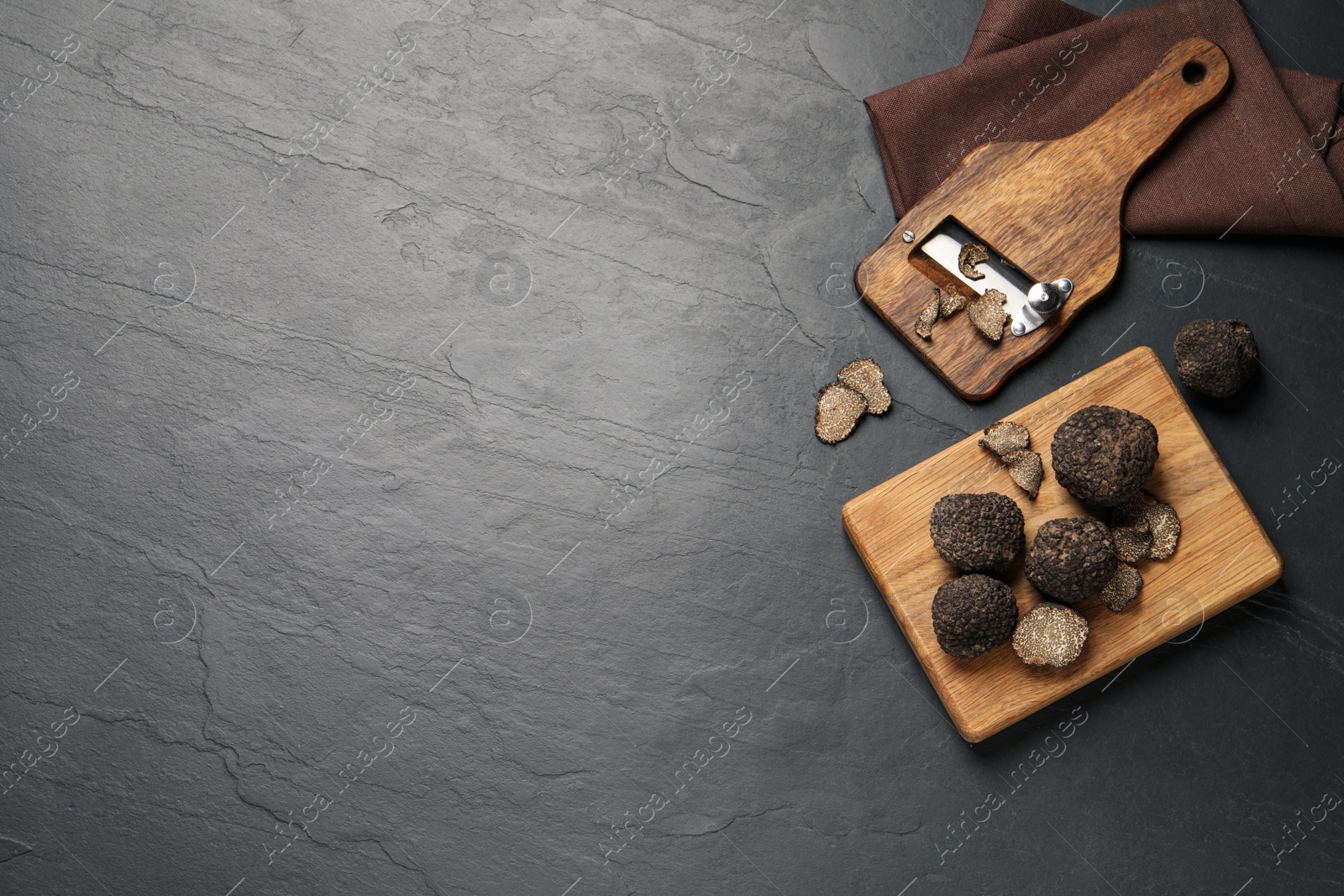 Photo of Wooden shaver with whole and sliced truffles on black table, flat lay. Space for text