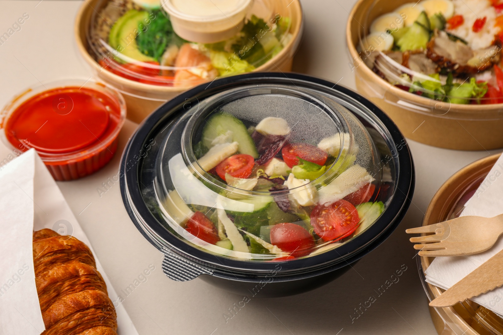 Photo of Tasty food in containers with wooden knife and fork on light grey table