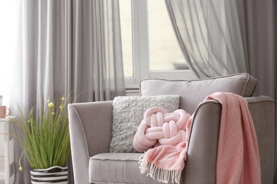 Pillows and plaid on armchair in room interior. Unusual cushion design